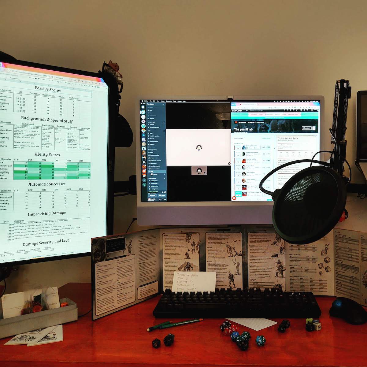 Two computer screens. A 5e DM screen several dice and a microphone